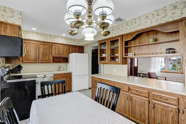 kitchen with black microwave, a notable chandelier, freestanding refrigerator, and wallpapered walls