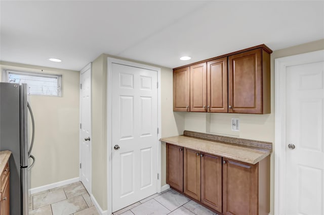 kitchen featuring brown cabinetry, light countertops, freestanding refrigerator, and baseboards