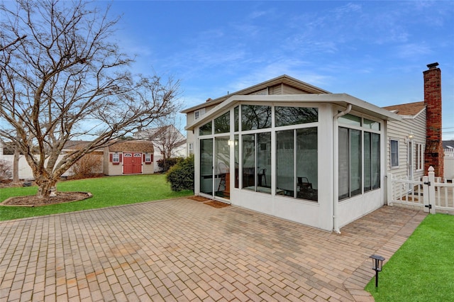 rear view of house with a lawn, a chimney, an outdoor structure, a sunroom, and a patio