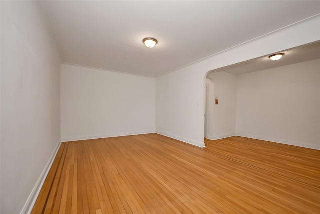 unfurnished room with arched walkways, light wood-style flooring, and baseboards