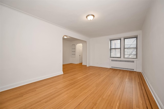 empty room with baseboards, arched walkways, radiator heating unit, and light wood finished floors