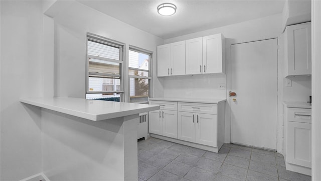 kitchen featuring white cabinets, radiator heating unit, a peninsula, light countertops, and a kitchen bar