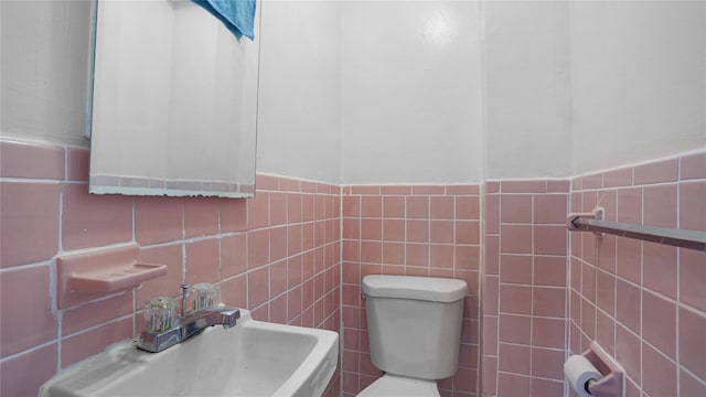 bathroom featuring a sink, tile walls, and toilet