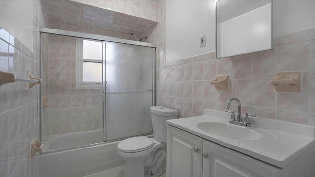 full bath with toilet, shower / bath combination with glass door, vanity, and tile walls