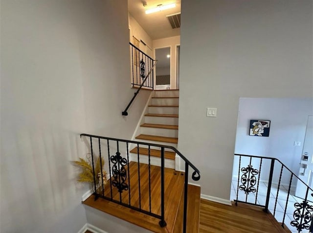 staircase featuring wood finished floors, visible vents, and baseboards