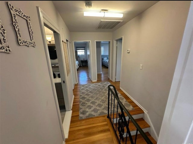 corridor featuring baseboards, visible vents, wood finished floors, and an upstairs landing