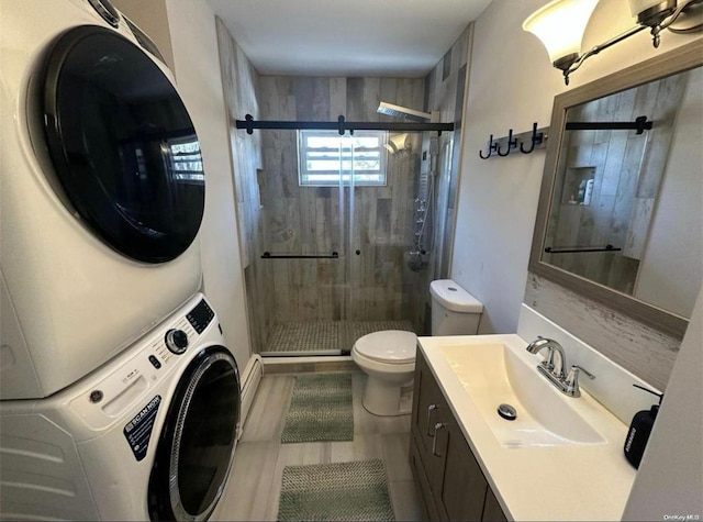 bathroom featuring toilet, a shower stall, stacked washer / dryer, and vanity