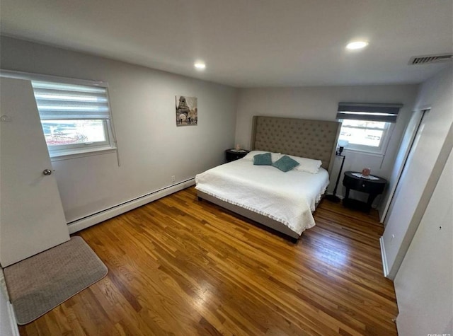 bedroom with a baseboard heating unit, recessed lighting, visible vents, and wood finished floors