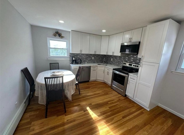 kitchen featuring light wood finished floors, stainless steel appliances, tasteful backsplash, a baseboard heating unit, and a sink