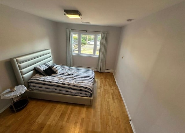 bedroom featuring a baseboard heating unit, visible vents, baseboards, and wood finished floors