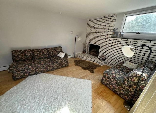 living area featuring baseboard heating, a brick fireplace, brick wall, and wood finished floors