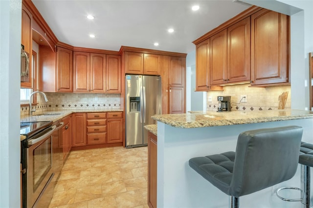 kitchen featuring a breakfast bar area, light stone countertops, a peninsula, a sink, and appliances with stainless steel finishes