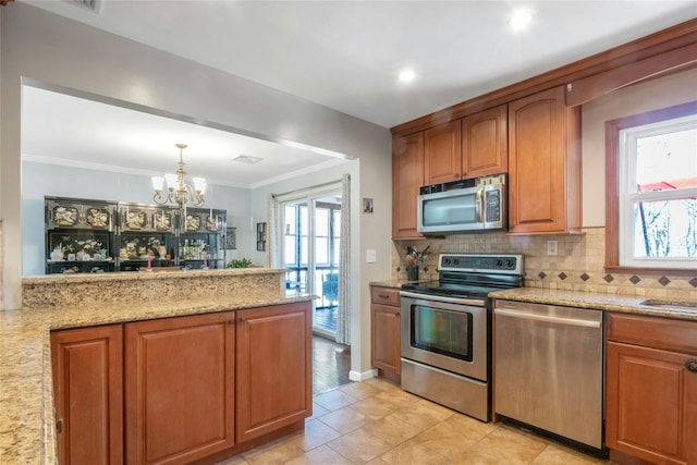 kitchen featuring brown cabinets, ornamental molding, light stone counters, backsplash, and appliances with stainless steel finishes