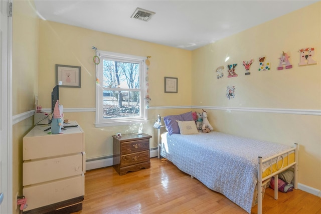 bedroom featuring visible vents, baseboard heating, a baseboard heating unit, and wood finished floors