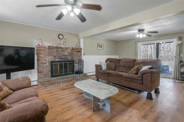 living area featuring a baseboard heating unit, a ceiling fan, wood finished floors, and a fireplace