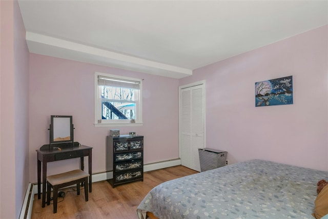 bedroom with a closet, baseboard heating, light wood-style flooring, and a baseboard heating unit