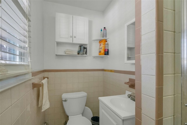 half bath with vanity, tile walls, toilet, and a wainscoted wall