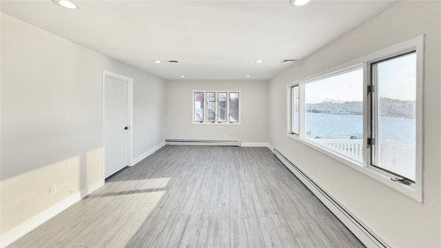 unfurnished room featuring a healthy amount of sunlight, light wood-style flooring, and a baseboard heating unit