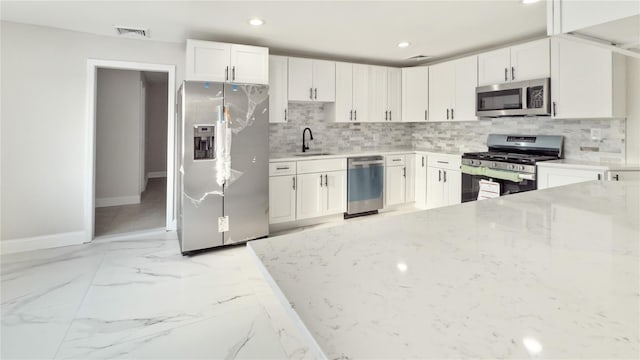 kitchen featuring light stone counters, stainless steel appliances, tasteful backsplash, visible vents, and a sink