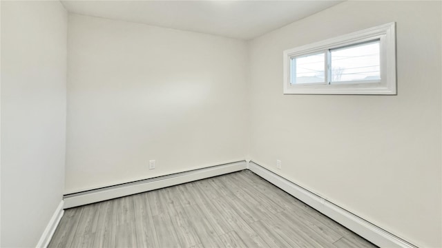 unfurnished room with a baseboard heating unit, light wood finished floors, and baseboards