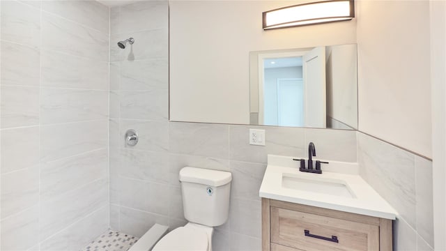 bathroom with tiled shower, vanity, toilet, and tile walls