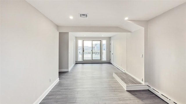 interior space with a baseboard heating unit, baseboard heating, wood finished floors, and visible vents