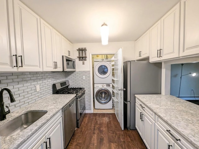 kitchen featuring stainless steel appliances, a sink, white cabinets, stacked washing maching and dryer, and dark wood finished floors