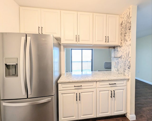 kitchen with white cabinetry, baseboards, light stone countertops, stainless steel fridge, and dark wood finished floors