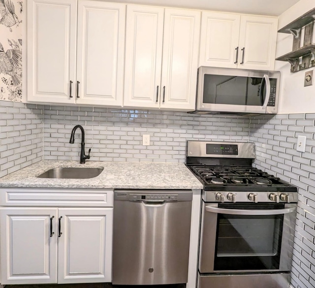 kitchen with appliances with stainless steel finishes, light stone counters, a sink, white cabinetry, and backsplash