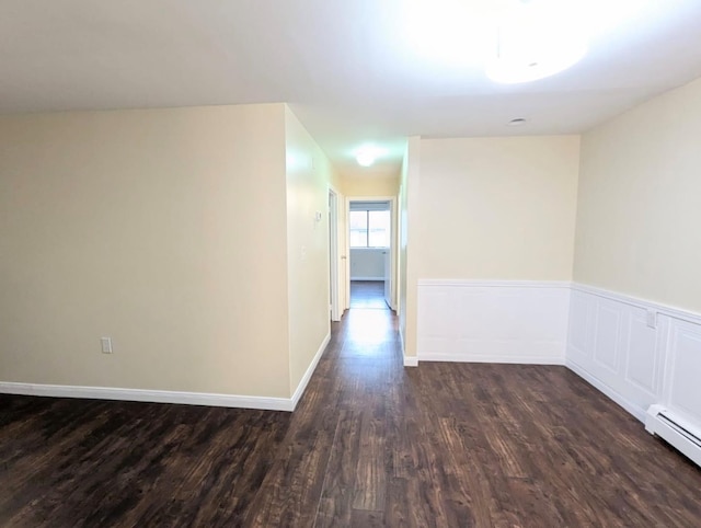 corridor featuring a baseboard heating unit, dark wood-type flooring, a wainscoted wall, and baseboards