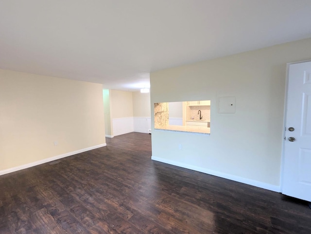 spare room featuring dark wood-style flooring, a sink, and baseboards