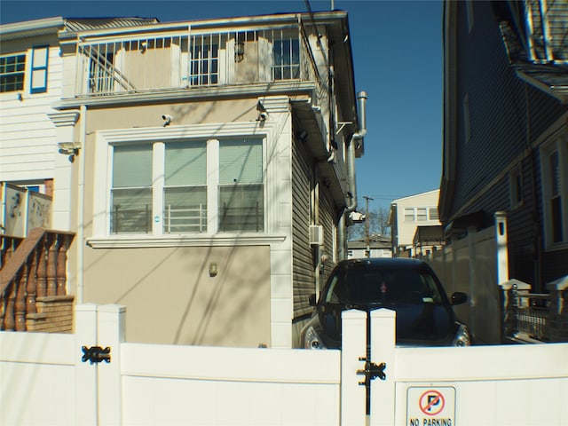 view of side of home featuring stucco siding, a balcony, and fence