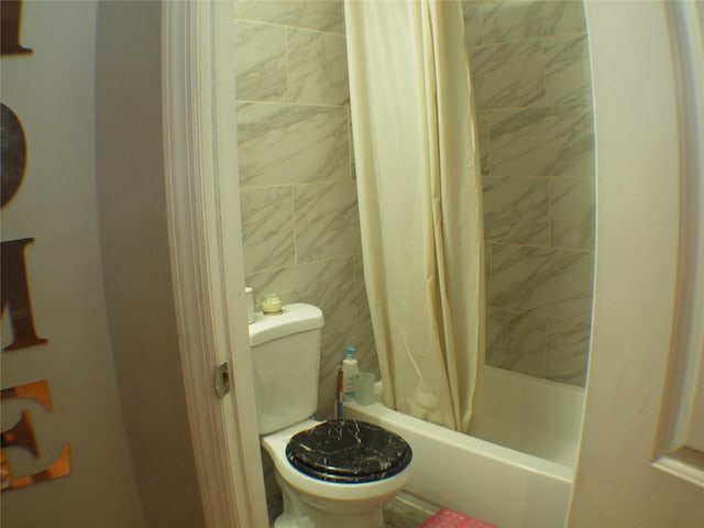 full bathroom featuring tiled shower / bath combo, toilet, and tile walls