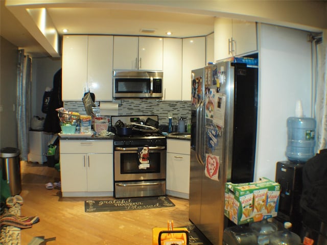 kitchen with light wood-type flooring, dark countertops, appliances with stainless steel finishes, white cabinets, and decorative backsplash