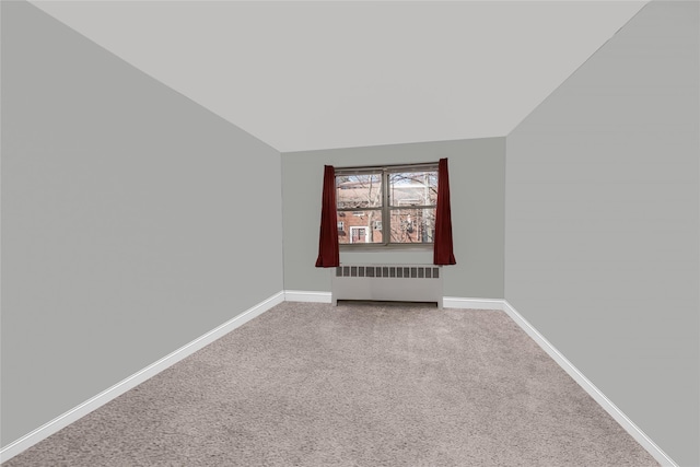 empty room with radiator, baseboards, carpet floors, and vaulted ceiling