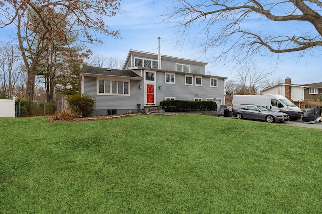 tri-level home featuring entry steps, fence, and a front lawn