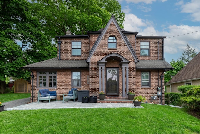 tudor-style house featuring brick siding, roof with shingles, and a patio area