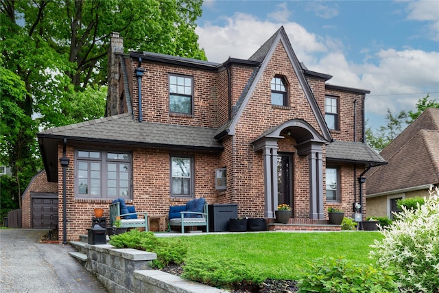 english style home with a front lawn, brick siding, a chimney, and a shingled roof