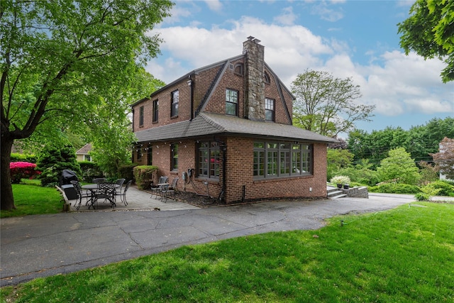 exterior space featuring a gambrel roof, a lawn, brick siding, a chimney, and a patio area