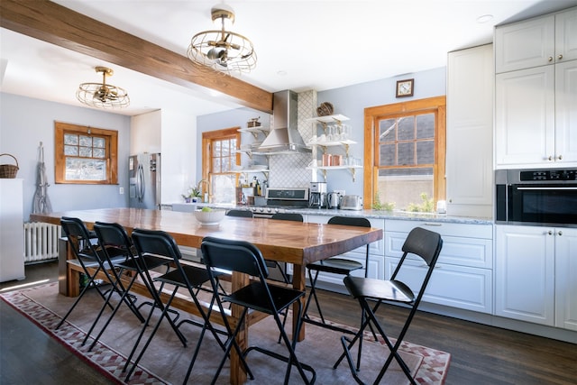 kitchen with plenty of natural light, radiator, stainless steel appliances, and wall chimney range hood