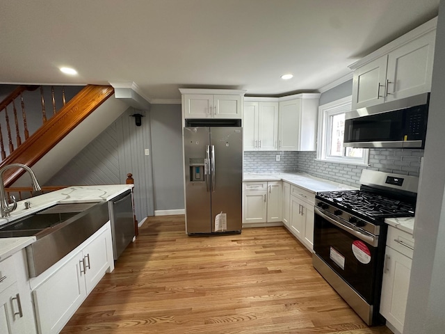 kitchen with stainless steel appliances, white cabinets, a sink, and light wood-style flooring