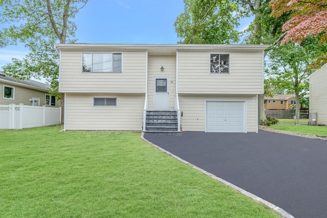 bi-level home featuring entry steps, an attached garage, fence, driveway, and a front yard