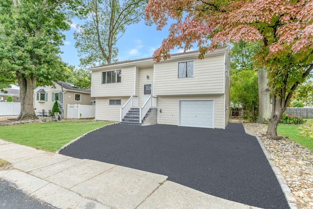 raised ranch with an attached garage, a front lawn, fence, and aphalt driveway