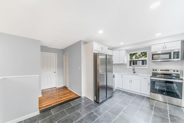 kitchen featuring stainless steel appliances, dark tile patterned floors, a sink, white cabinets, and light countertops