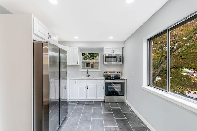 kitchen with stainless steel appliances, light countertops, white cabinets, a sink, and baseboards