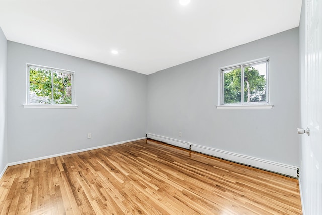 spare room featuring baseboards, plenty of natural light, baseboard heating, and wood finished floors