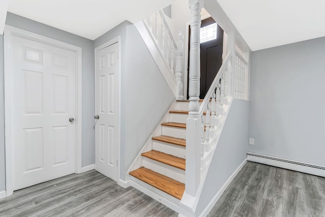 stairs with a baseboard radiator, wood finished floors, and baseboards