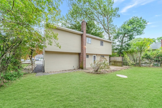 back of house featuring a gate, a yard, a chimney, and fence