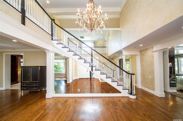 stairs with wood finished floors, a towering ceiling, and ornate columns