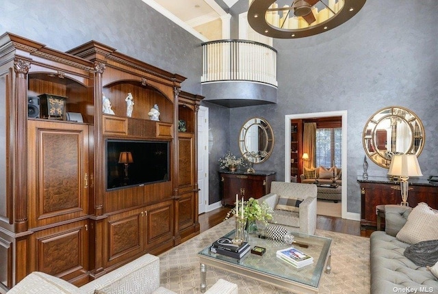 living area featuring ornamental molding, wood finished floors, a towering ceiling, and baseboards